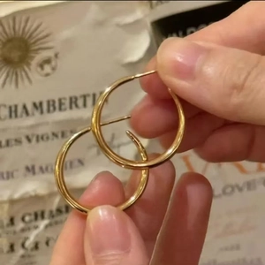 Classic gold minimalist hoop earrings shown being held against a vintage paper background