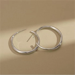 Close-up of minimalist silver hoop earrings with a polished mirror finish on a warm background