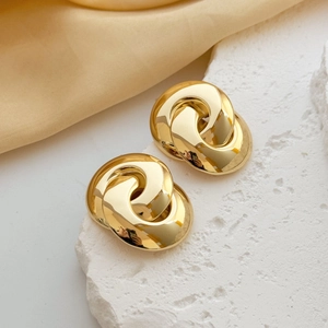 Macro detail of gold-tone interlocking geometric earrings on a white stone tray