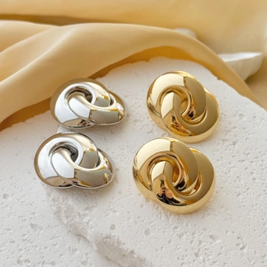 Macro detail of intertwined gold and silver knot hoop earrings on a stone textured surface