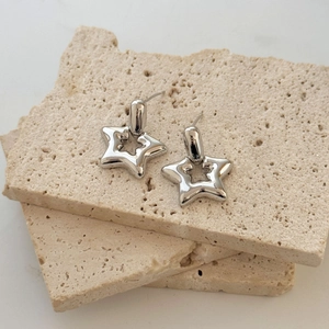 Modern hollow star earrings in polished silver finish on a minimalist stone texture