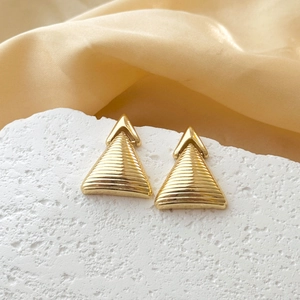 Macro shot of gold teardrop earrings with textured horizontal stripes on stone surface