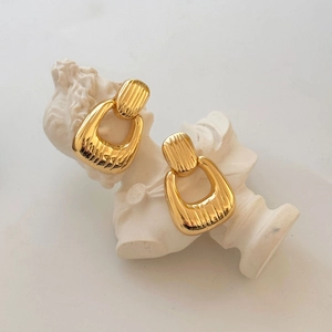Chic gold textured hoop earrings with vertical stripes on a classic white sculpture base