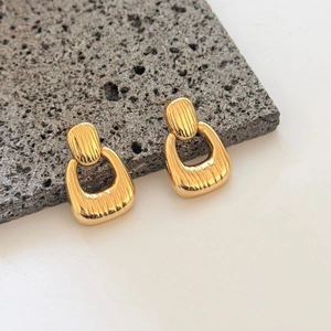 Macro detail of U-shaped gold earrings with vertical ribbed texture on stone surface