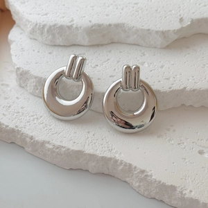 Close-up of chunky silver geometric hoop earrings with polished finish on white stone