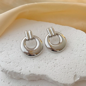 Polished silver geometric hoop earrings on stone pad with soft silk background