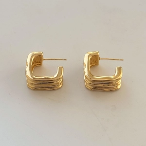 Detailed view of chunky golden C-shaped hoop earrings with layered wave textures