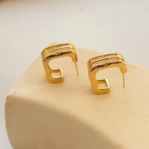 Minimalist gold geometric C-shaped hoop earrings with lava texture on a beige pedestal