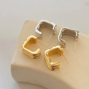 Close-up of gold and silver C-shaped geometric earrings with liquid metal texture on stone
