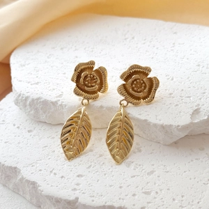Elegant gold flower and leaf tassel earrings displayed on white stone with fabric