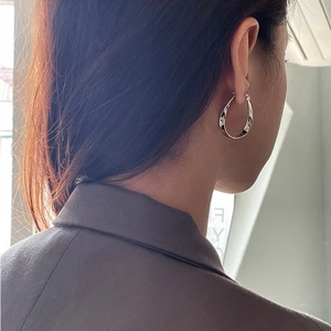 Minimalist Mobius hoop earrings in silver metal with twisted fluid design on model