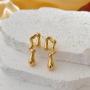 Modern geometric irregular liquid gold metal drop earrings on white stone pedestals