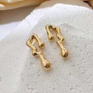 Close-up of golden hollow irregular fluid earrings on white textured stone stand