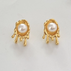 Detailed view of irregular molten gold stud earrings with white pearls on a white background