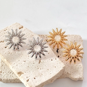 Fashionable gold and silver sun flower stud earrings set on a textured beige stone background
