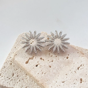 Close-up of silver sunflower earrings with polished petals on travertine stone base