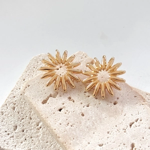Macro view of polished golden sunflower stud earrings on textured stone background