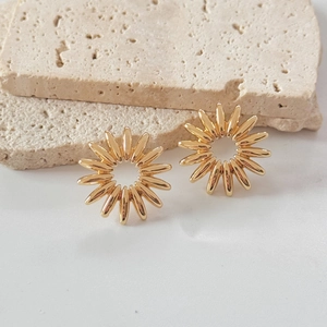 Polished gold sunflower stud earrings with a 3D hollow design on a stone background