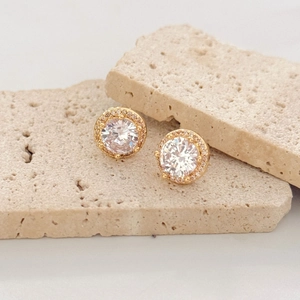 Elegant four-prong round zircon stud earrings in gold finish on natural stone