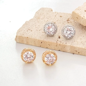 Macro detail of gold and silver four-claw round zircon stud earrings on stone stand