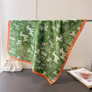 Close-up of green silk scarf featuring abstract animal prints and orange hem borders