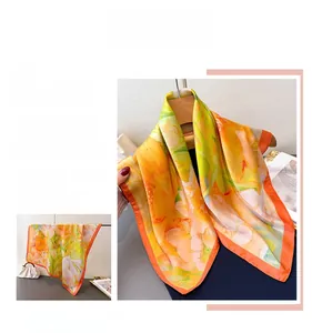 Detail of silk-like square scarf featuring orange and yellow floral patterns with orange borders