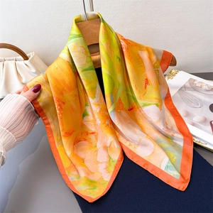 Vibrant floral silk scarf in orange and yellow draped elegantly on a wooden hanger