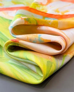 Macro detail of abstract floral silk-like scarf featuring vibrant satin texture and orange edges