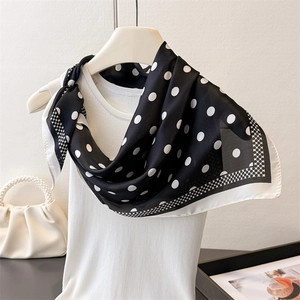 Elegant black and white polka dot silk scarf draped on a white vest with classic patterns