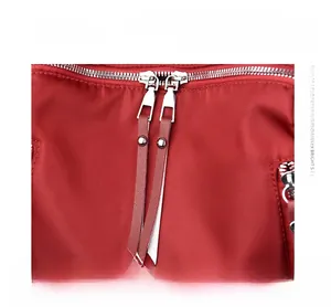 Detail of red nylon backpack showing double metal zippers and cowhide leather pullers