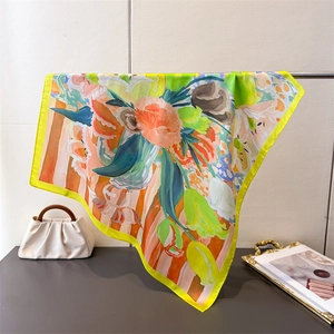 Elegant satin square scarf with bright floral prints draped on a metal stand with a chic bag