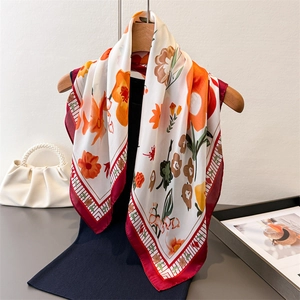 Floral faux silk square scarf in cream and orange with red border on a wooden hanger