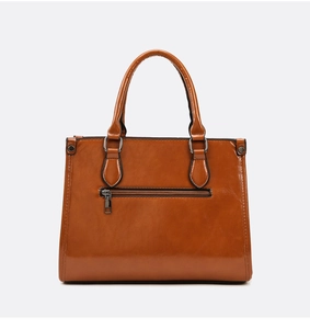 Détail d'un sac cabas en cuir verni marron avec poche zippée frontale et ferrures en métal
