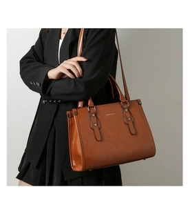 Détail du sac cabas en cuir verni marron avec logo doré et boucles décoratives