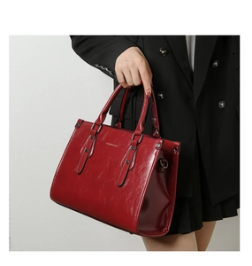 Détail d'un sac à main en cuir verni rouge avec doubles poignées et boucles dorées