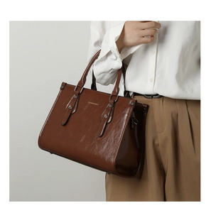 Détail d'un sac cabas marron en cuir verni montrant la texture et les boucles argent