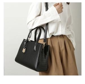 Detail of black crocodile embossed tote bag showing side texture and golden hardware