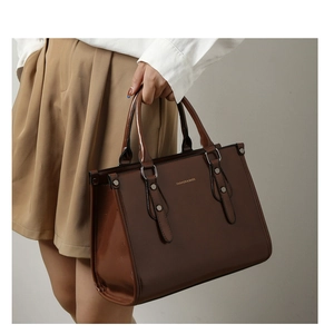 Gros plan sur le sac fourre-tout en cuir verni marron avec anneaux et texte doré