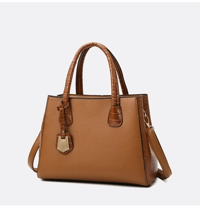Close-up of brown textured handbag featuring crocodile embossed trim and gold metal buckle
