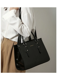 Sac fourre-tout en cuir verni noir porté avec logo doré et détails rivetés