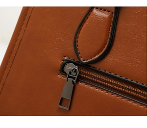 Détail de la fermeture éclair bronze et des coutures sur un sac en cuir verni marron