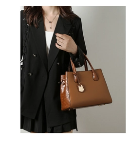 Close-up of brown crocodile embossed leather tote with gold hardware and logo charm