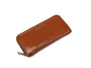 Détail d'un portefeuille long en cuir verni marron avec logo doré et zip métallique