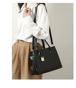 Detailed view of black crocodile pattern tote bag with gold hardware on a model