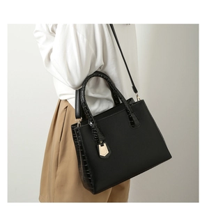 Detail of black faux crocodile leather tote with gold hardware and contrast textures