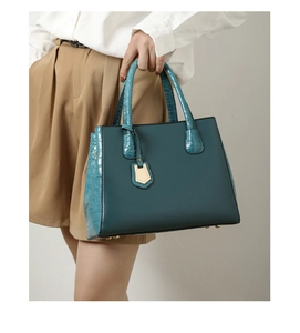 Detail of teal faux leather handbag with crocodile pattern texture and golden feet