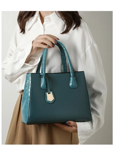 Detail of teal tote bag featuring crocodile embossed texture and gold metal pendant
