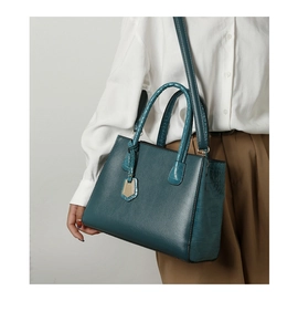 Detail of teal leather handbag featuring crocodile embossing and gold metal tag hardware
