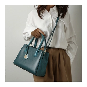 Detail of crocodile embossed leather and gold hardware on dark green tote bag