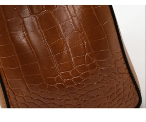 Macro shot of dark brown crocodile embossed leather texture with detailed black edge finish